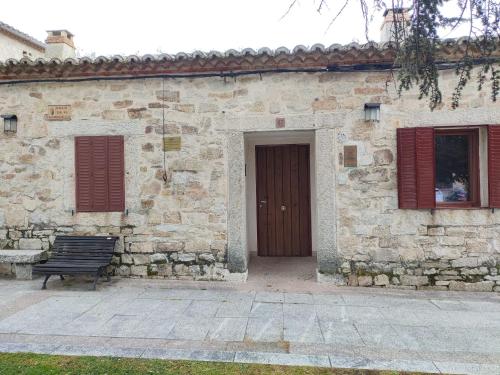 un edificio in pietra con una porta in legno e una panca di Alojamiento Antigua Casa de Telefonos a El Berrueco