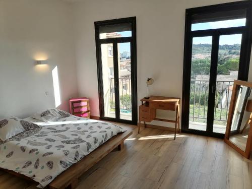 a bedroom with a bed and a desk and windows at Maison spacieuse & chaleureuse au cœur du village in Cases-de-Pène