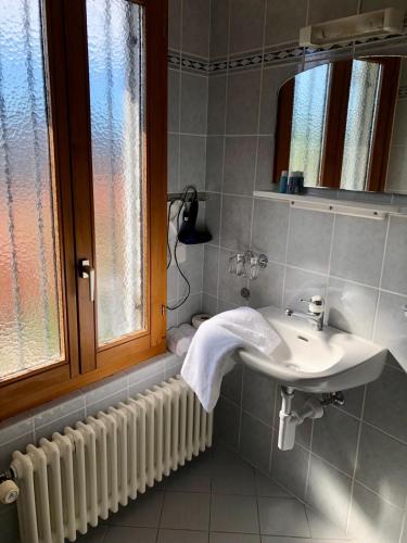 La salle de bains est pourvue d'un lavabo, d'un miroir et d'une fenêtre. dans l'établissement Ristorante Bar Pensione Novaggio, à Novaggio