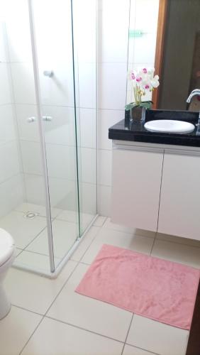 uma casa de banho com um chuveiro, um lavatório e um tapete rosa em Clenilda na Praia Grande