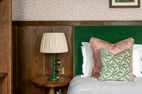 a bedroom with a bed with a green headboard and a lamp at Worplesdon Place Hotel in Guildford