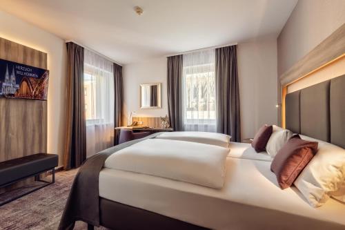 a hotel room with a large white bed and windows at CityClass Hotel am Dom in Cologne