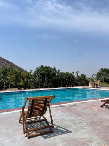 a wooden chair sitting next to a swimming pool at Farm Aavjo - A Conscious Stay in Pushkar