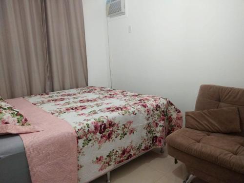 a bedroom with a bed with a flowered blanket and a chair at Apartamento com otima localizacao em Itajai SC in Itajaí