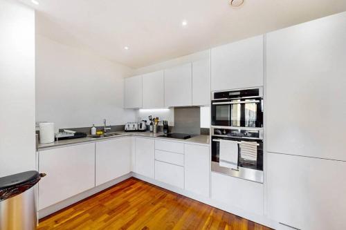 a white kitchen with white cabinets and a wooden floor at 2Bed & 2Bath Flat w free parking, lift, balcony in London