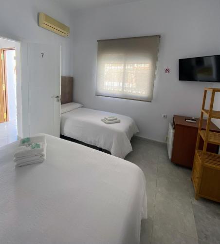 a white room with two beds and a television at Hostal Avenida by Bossh! Hotels in Chipiona