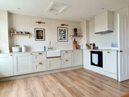 uma grande cozinha com armários brancos e pisos de madeira em Trinity Square Loft + sea views em Kent