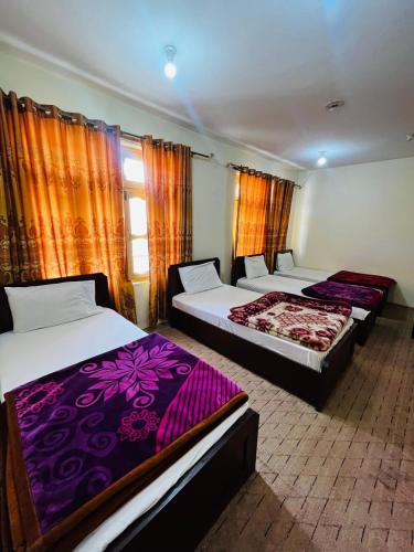 two beds in a room with orange curtains at Heaven Hotel Skardu in Skardu