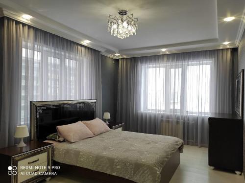 een slaapkamer met een bed, een kroonluchter en ramen bij Уютная квартира на Кадыр-Мырза Али in Oral