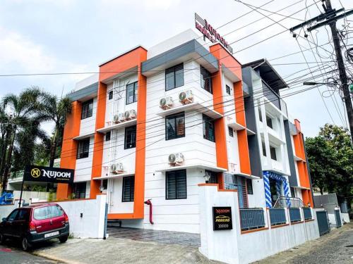 a white and orange building with a car parked in front at Nujoom Apartments in Ernakulam