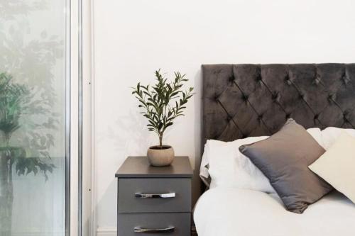a plant on a night stand next to a bed at Parkside Haven, Modern 2-Bed Flat with Ensuites, Free Parking & Self Check-In in Perivale