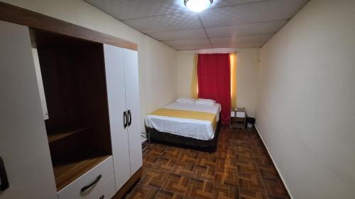 Yanira's house في سانتا آنا: غرفة نوم صغيرة بسرير وستارة حمراء