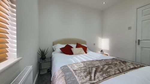 um quarto com uma cama com lençóis brancos e almofadas vermelhas em Highfield House! em Wellingborough