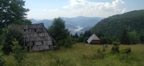 two old barns in a field with mountains in the background at Vikendica Studenac in Bajina Bašta