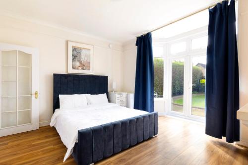a bedroom with a large bed with blue curtains at Detached 4-Bed House near Heathrow in Egham