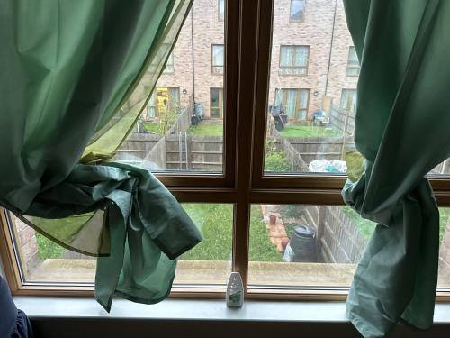una ventana con cortinas verdes y vistas a un patio en Bedsit room, en Thamesmead