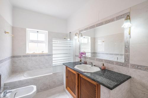 a bathroom with a sink and a tub and a mirror at Villa Glória in Praia do Carvoeiro