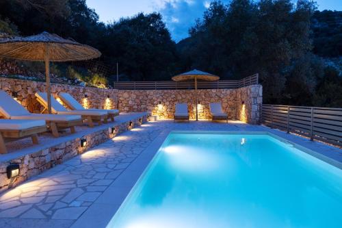 a pool with chairs and umbrellas at night at Paradise Villas in Sami