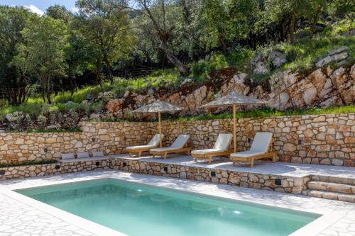 a pool with chairs and umbrellas next to a stone wall at Paradise Villas in Sami