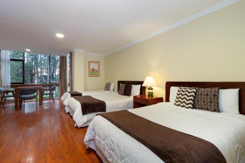 two beds in a hotel room with a table and chairs at Hotel NASS Pinar del Lago in Cuenca