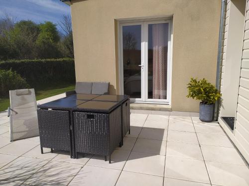 a patio with a table and a chair in front of a door at Chambre entre mer et campagne in Gréville-Hague