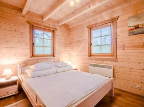 a bed in a wooden room with two windows at Charmantes Ferienhaus in Dbina mit Offenerem Kamin und Strand in der Nähe in Debina