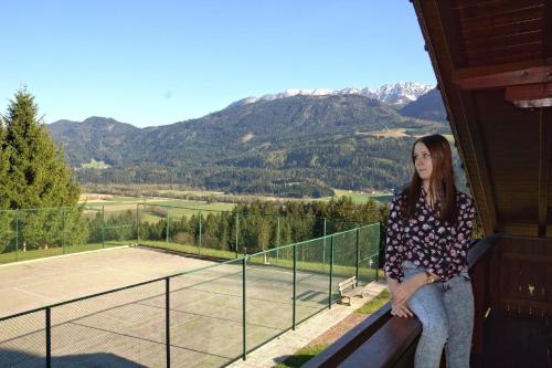 a woman sitting on a balcony with a tennis court at Holzblockhaus auf zwei Etagen mit Whirlbadewanne und Kaminofen in Berg im Drautal