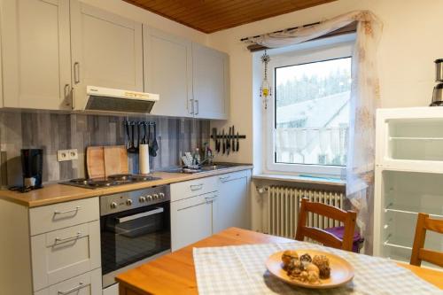 eine Küche mit weißen Schränken, einem Tisch und einem Fenster in der Unterkunft Ferienwohnung auf einem Reiterhof in Weißenstadt