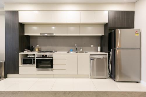 una cocina con armarios blancos y electrodomésticos de acero inoxidable en Comfortable apartment, near Parramatta CBD!, en Merrylands