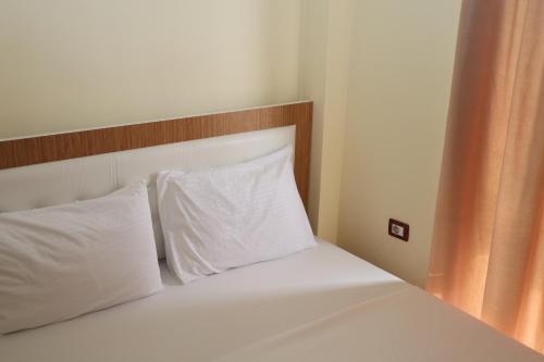 1 cama con 2 almohadas blancas y cabecero de madera en Gusto Hotel, en Ksamil