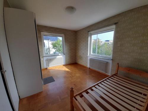 an empty room with a bed and two windows at Room in house with good communication in Stockholm