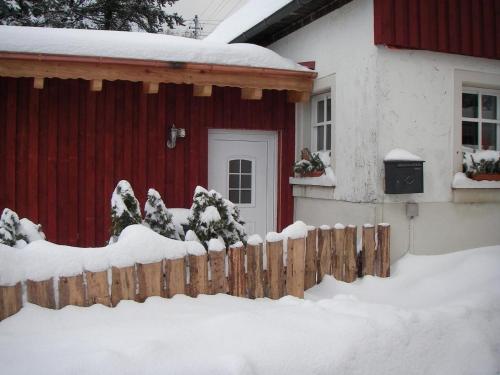 a red house with a fence covered in snow at Ferienhaus "Lena" in Presseck