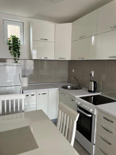 a kitchen with white cabinets and a sink and a table at Apartman Dragovic in Kuršumlija