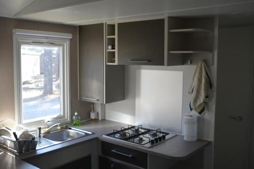 a kitchen with a stove and a sink and a window at Hébergement dans un camping de rêve in Vendays-Montalivet