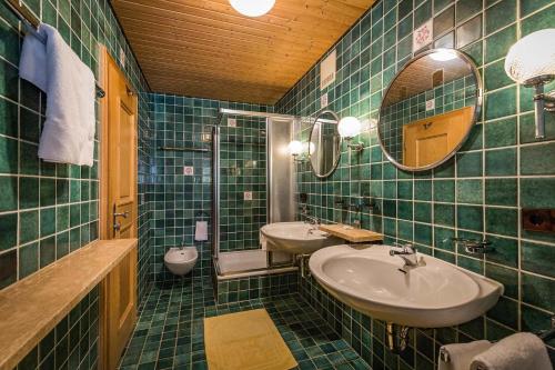 a green tiled bathroom with two sinks and a mirror at Landhotel Sonnleiten in Bad Reichenhall