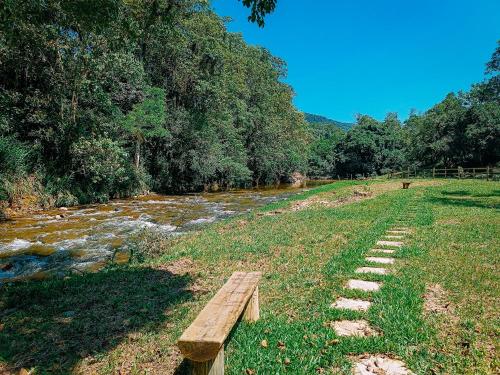 a wooden bench sitting next to a river at Suíte com cachoeira no quintal in Antônio Carlos