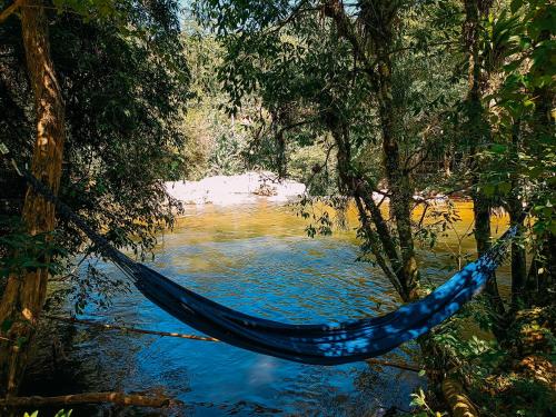 a hammock in a forest next to a river at Suíte com cachoeira no quintal in Antônio Carlos