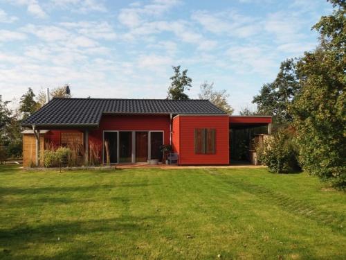 una casa roja con un césped verde delante de ella en Ferienhaus am kleinen See mit Steg, Garten und Terrasse en Twist