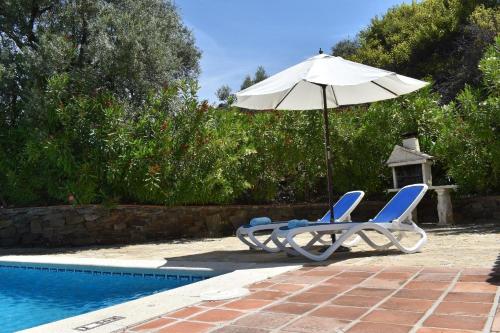 un par de sillas y una sombrilla junto a una piscina en Ferienhaus mit Privatpool für 4 Personen ca 120 qm in Corumbela, Andalusien Costa del Sol, en Sayalonga