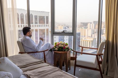 einem Mann, der in einem Zimmer mit Fenster auf einem Stuhl sitzt in der Unterkunft Wassad Hotel Makkah فندق وسد مكة in Mekka