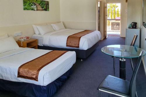 パースにあるEcono Lodge Rivervaleのベッド2台とガラスのテーブルが備わるホテルルームです。