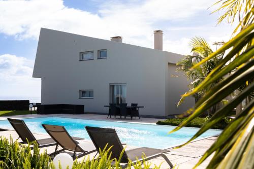 a villa with a swimming pool and chairs at J&B Place in Ponta Delgada