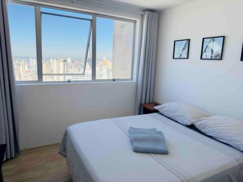 um quarto com uma cama e uma grande janela em A melhor opção no centro com vista panorâmica em Curitiba