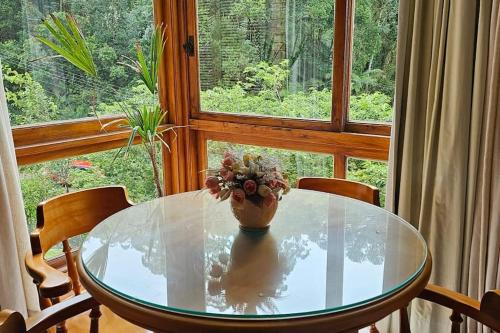 a glass table with a vase with flowers on it in front of a window at Melhor localização de Gramado in Gramado
