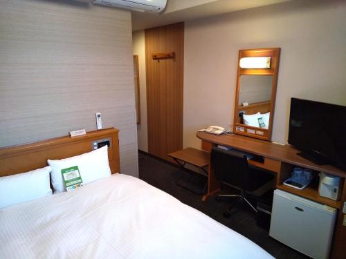 a hotel room with a bed and a desk with a mirror at Hotel Route-Inn Odate Omachi in Odate