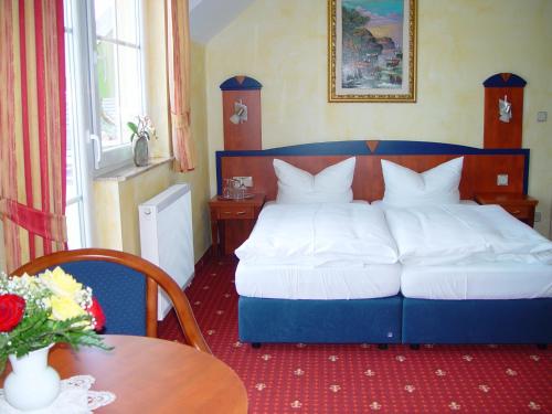 a bedroom with a blue bed with white sheets and a table at Hotel Ostseeblick - direkt hinter den Dünen in Ostseebad Karlshagen