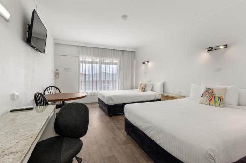 um quarto de hotel com duas camas, uma secretária e uma cadeira em Zebra Motel em Coffs Harbour