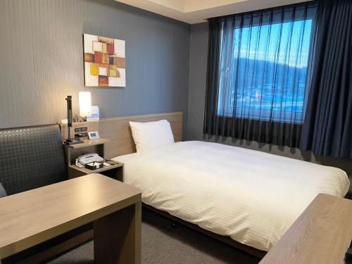 a hotel room with a bed and a desk and a window at Hotel Route-Inn Yamagata South - in front of University Hospital - in Yamagata