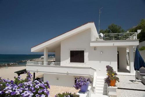 una casa blanca en la playa con flores púrpuras en Ferienhaus für 6 Personen ca 80 qm in Trappeto, Sizilien Nordküste von Sizilien, en Trappeto