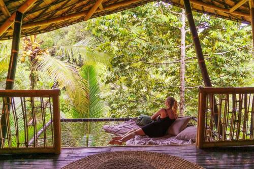 a woman sitting on a bed on a porch at Eco Bamboo Island Bali - Bamboo House #4 in Selat